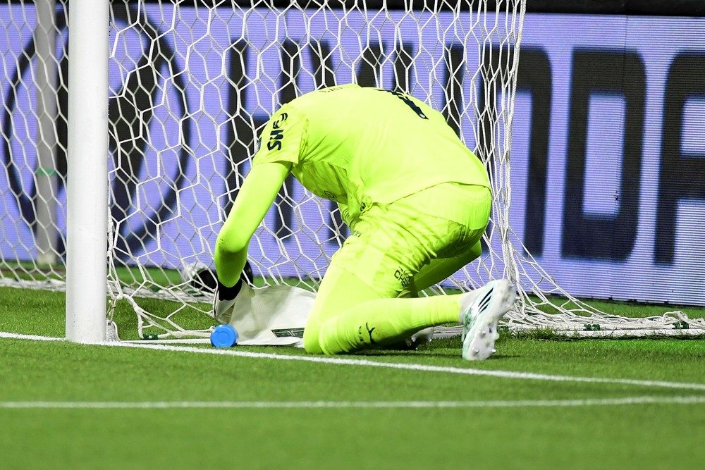 Carlos Miguel, goleiro do Palmeiras, de uniforme verde-limão, ajoelhado junto à trave e de costas para a câmera, mexe numa toalha branca estendida no gramado do Nubank Parque