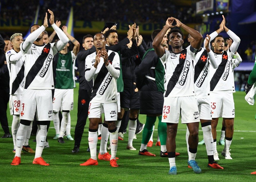 Jogadores do Vasco, de camisa branca com a faixa diagonal preta, aplaudem com os braços erguidos no gramado da Bombonera