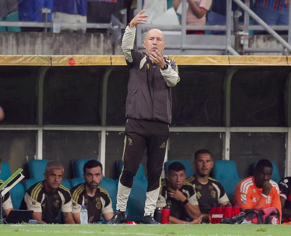 Leonardo Jardim, de agasalho escuro do Flamengo, gesticula à beira do campo com o braço direito erguido, com reservas rubro-negros sentados no banco atrás dele